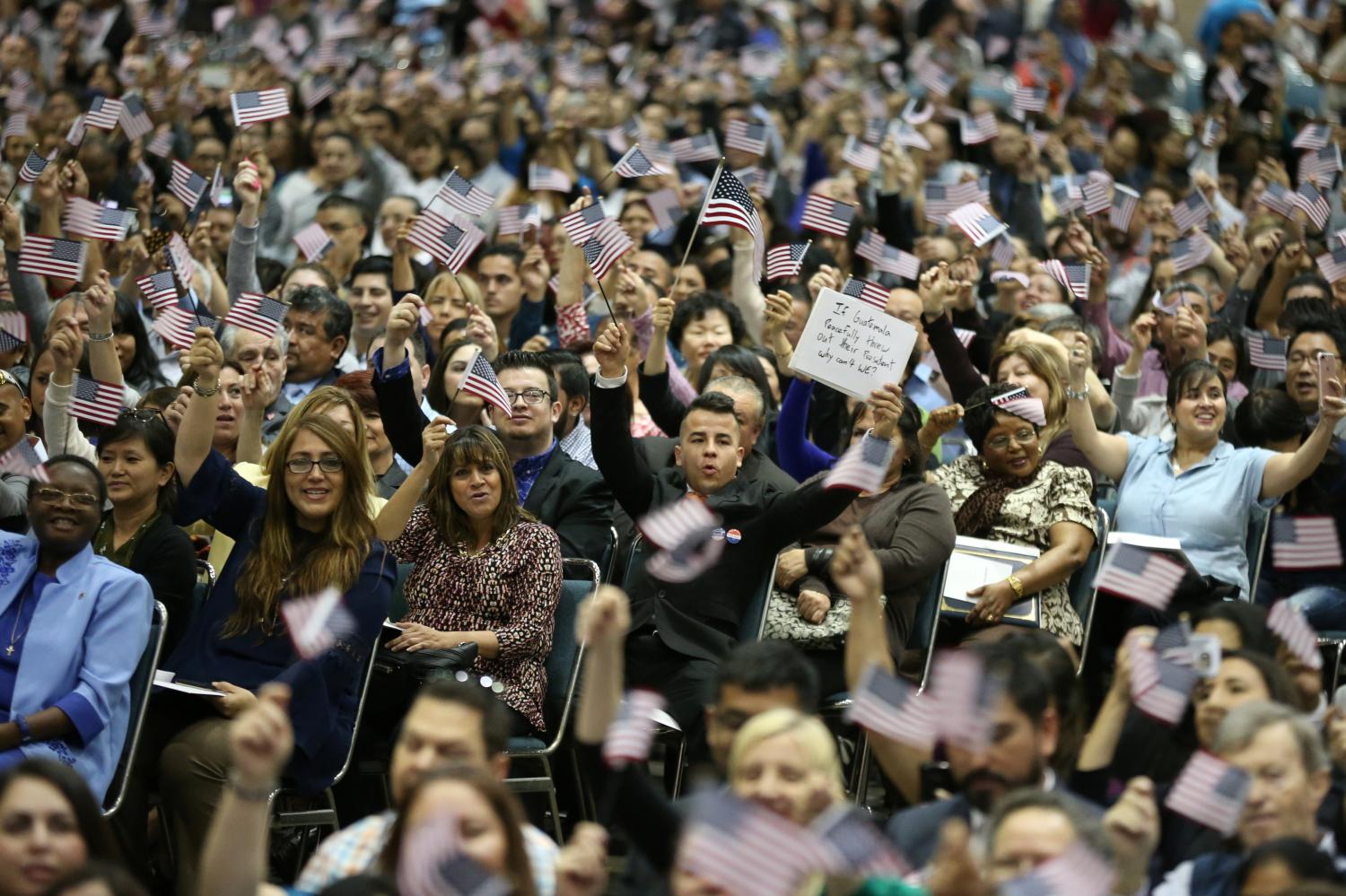 New U.S. citizen Juan Rosales, 24, who emigrated from Guatemala when he was 8, holds up a protest sign reading "If Guatemala peacefully threw out their president why can't WE?" after a naturalization ceremony for thousands of new U.S. citizens from various countries, in Los Angeles