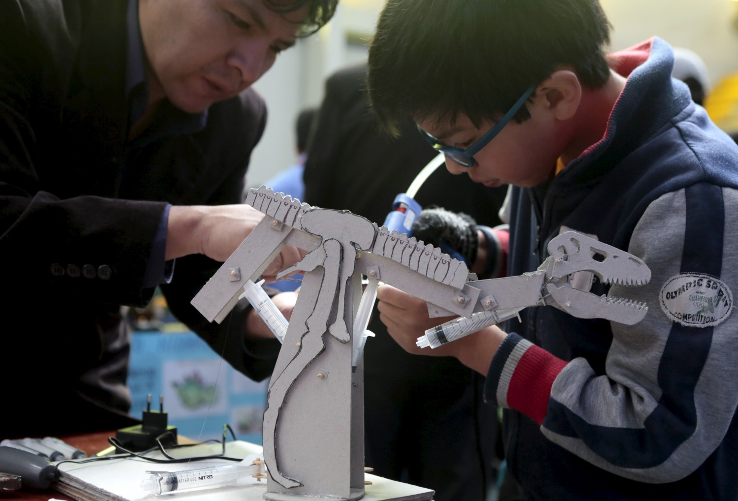 A student is helped by his teacher to build a dinosaur robot during the annual robotics fair supported by the Bolivian Education Ministry in La Paz