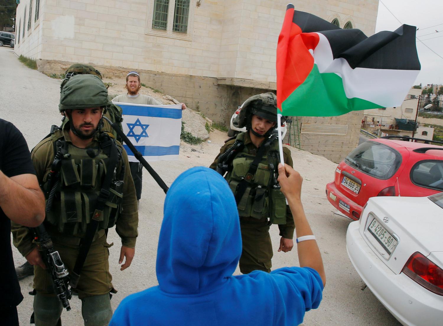 Demonstrator holds a Palestinian flag in front of Israeli troops during a protest marking Land Day in the West Bank city of Hebron
