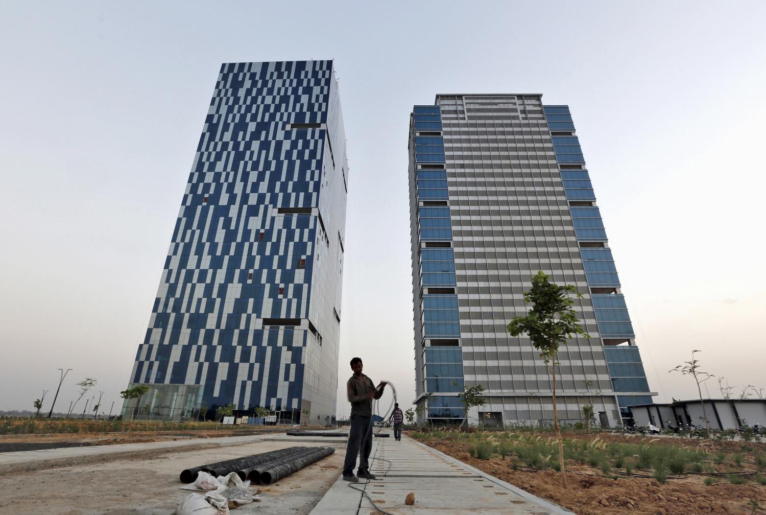 A worker folds cable of welding machine in front of two office buildings at Gujarat International Finance Tec-City at Gandhinagar, in Gujarat