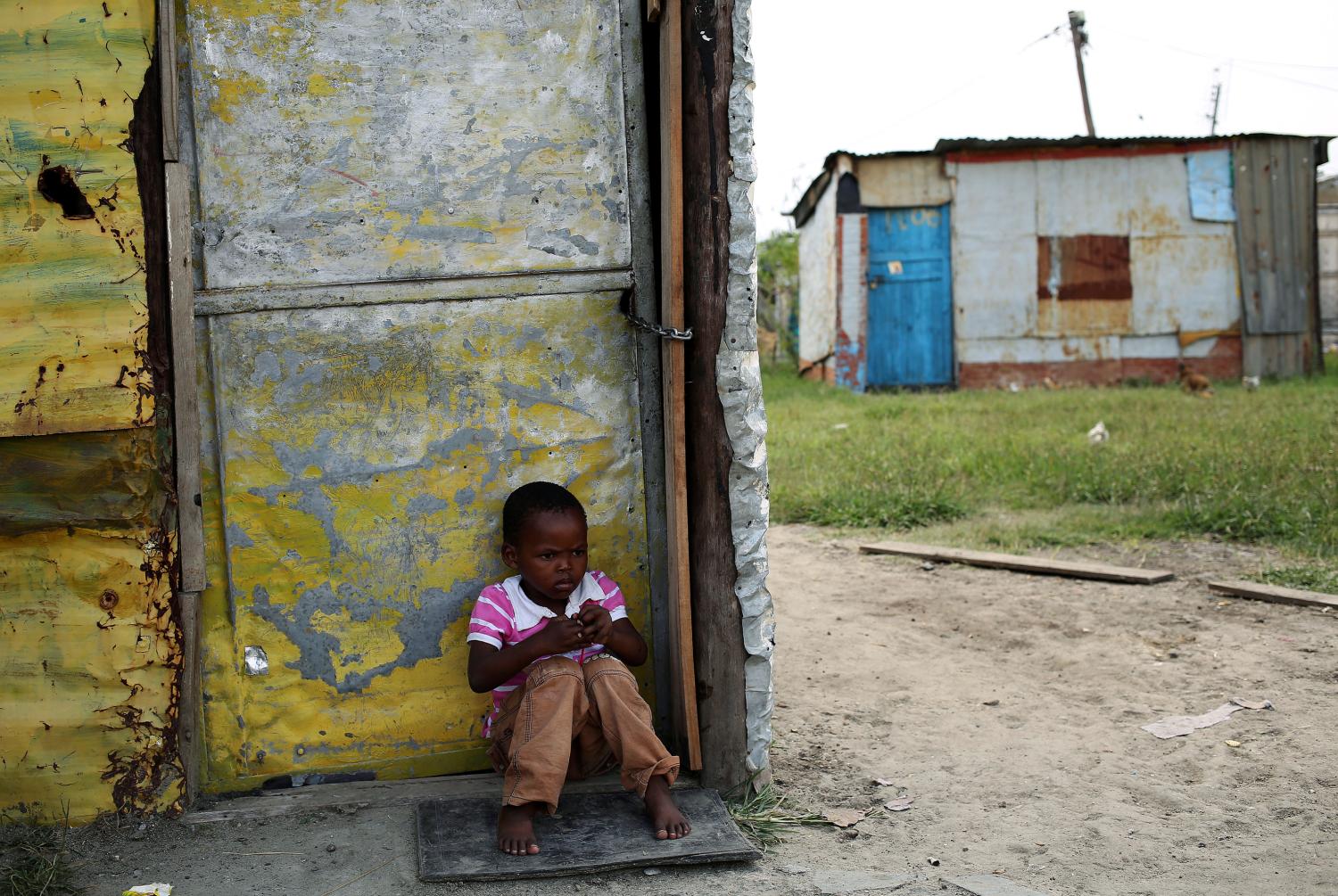A child sits outside a locked shack in Nkaneng township, Marikana's informal settlement, in Rustenburg