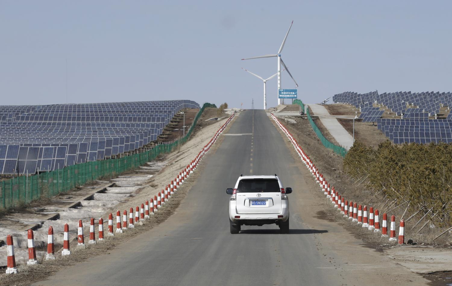 A vehicle drives past the solar panels near wind turbines at a wind and solar energy storage and transmission power station in Zhangjiakou