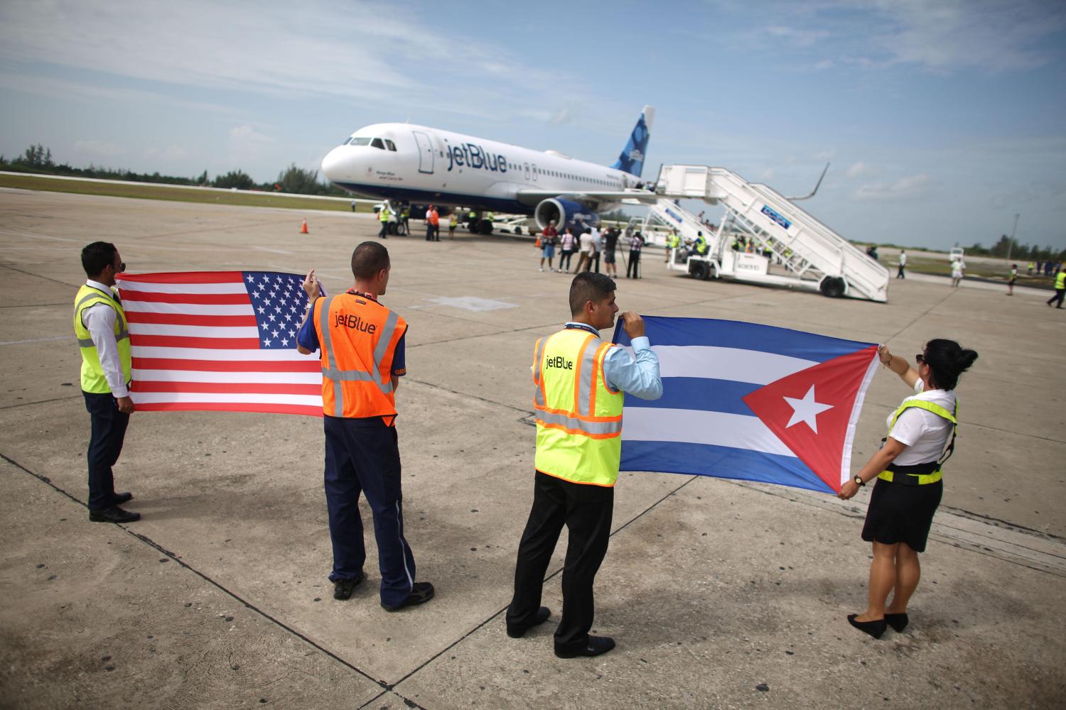 Ground crew hold U.S. and Cuban flags near a recently landed JetBlue aeroplane, the first commercial scheduled flight between the United States and Cuba in more than 50 years, at the Abel Santamaria International Airport in Santa Clara, Cuba, August 31, 2016. REUTERS/Alexandre Meneghini - RTX2NQET