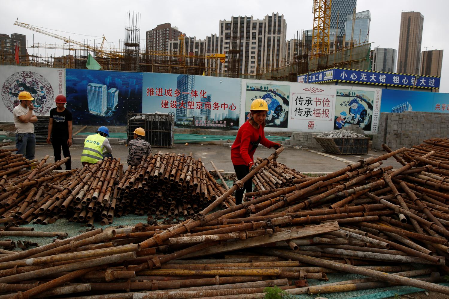 A woman sorts scaffolding poles at a construction site near recently erected office and residential high-rises in Beijing, China April 20, 2017. REUTERS/Thomas Peter - RTS1342V