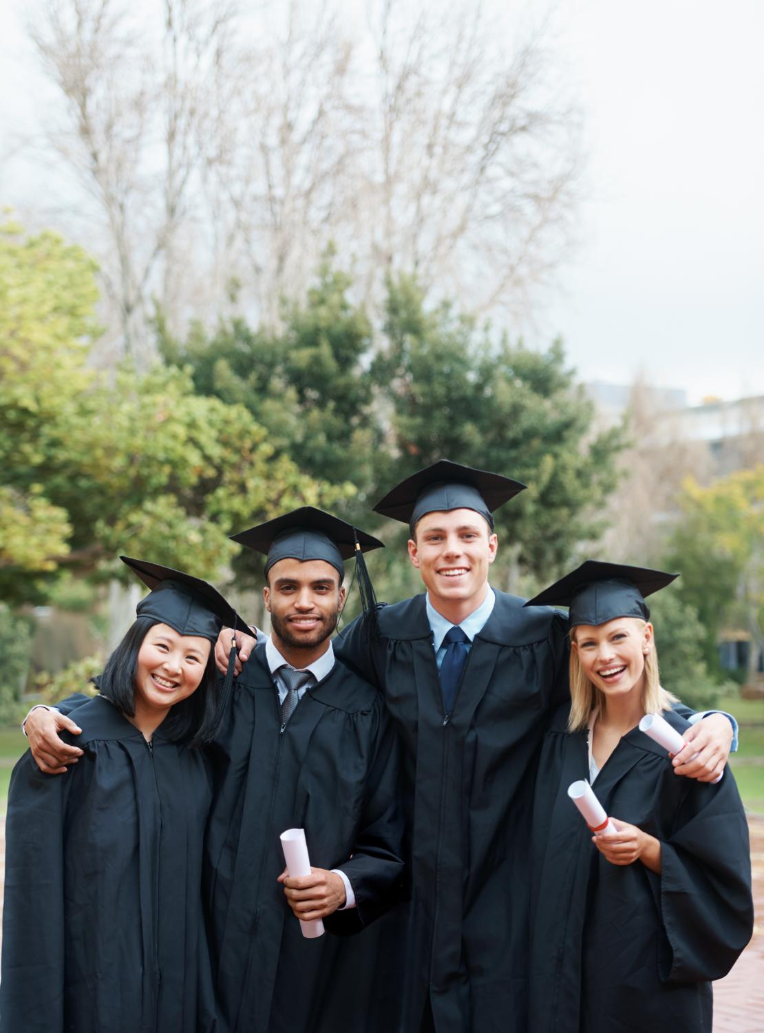 A group of college graduates standing in cap and gown and holding their diplomas