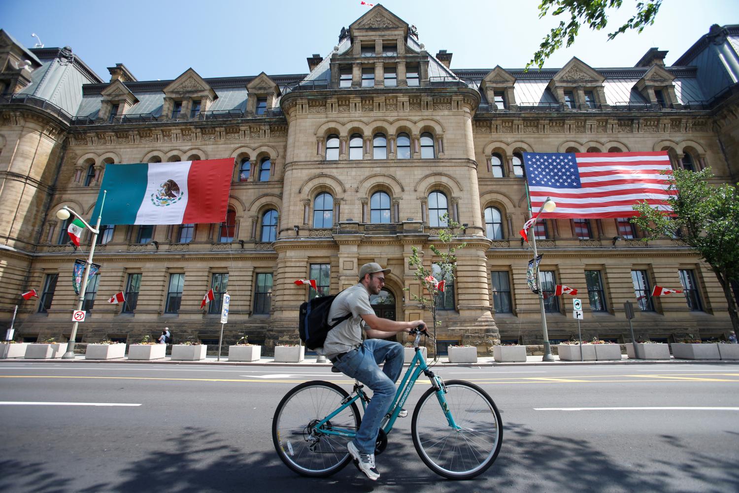 The Mexican and U.S. flags hang from the Langevin Block in advance of Wednesday's North American Leaders' Summit as a cyclist passes by in Ottawa, Ontario, Canada, June 27, 2016. REUTERS/Chris Wattie - RTX2IK28