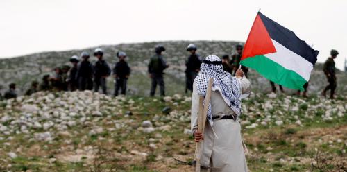 A man holds a Palestinian flag in front of Israeli troops during a protest marking Land Day in the West Bank village of Madama, near Nablus March 30, 2017. REUTERS/Mohamad Torokman - RTX33DP8