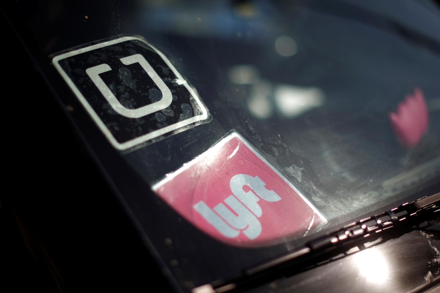 The corporate logos of Uber and Lyft are displayed on a driver's windshield.