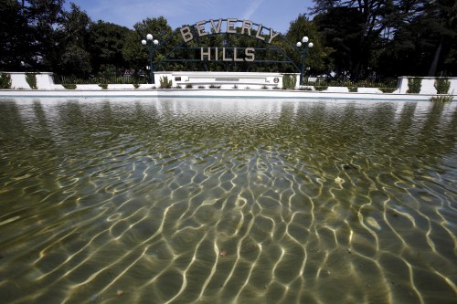 Water is seen in a pond in front of Beverly Hills' city sign