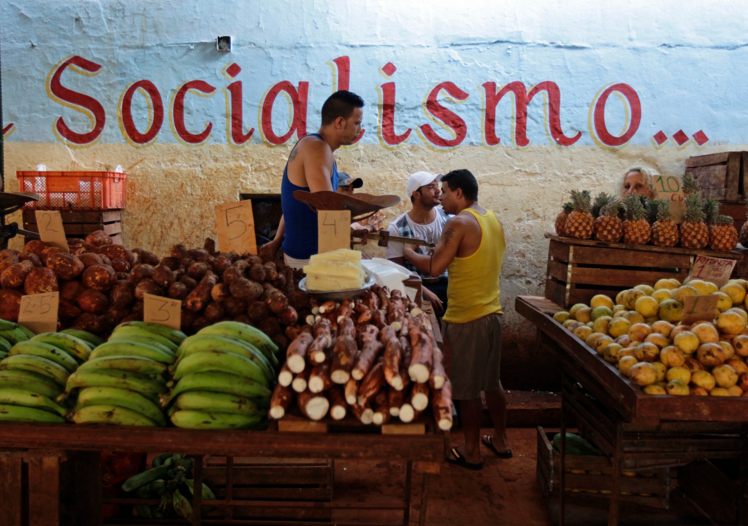 Vendors wait for customers at their stalls, with prices tagged in Cuban pesos, at a market in Havana October 23, 2013. Cuba took the first step towards scrapping its two-tier currency on October 22, 2013, in a move which could boost local workers' income and remove a major hurdle for importers and exporters. Cuba's convertible peso (CUC) is pegged to the U.S. dollar, while the local peso (CUP) is valued at a fraction of the greenback's value, angering the population which is paid in the latter, and complicating accounting, the evaluation of performance, and trade for state companies. The writing on the wall in the background reads, "Socialism". REUTERS/Desmond Boylan (CUBA - Tags: SOCIETY BUSINESS AGRICULTURE) - RTX14LG0
