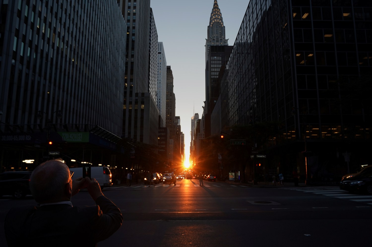 A man takes a photo as the sun sets while lined up with 42nd Ave a few days after the Manhattanhenge phenomenon.