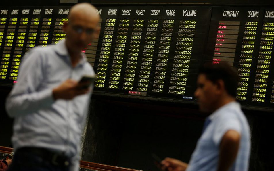 Men use their cell phones as they stand in front of electronic board displaying share market prices during a trading session in the halls of Pakistan Stock Exchange (PSX) in Karachi, Pakistan ?June 12, 2017. REUTERS/Akhtar Soomro - RTS16OE0