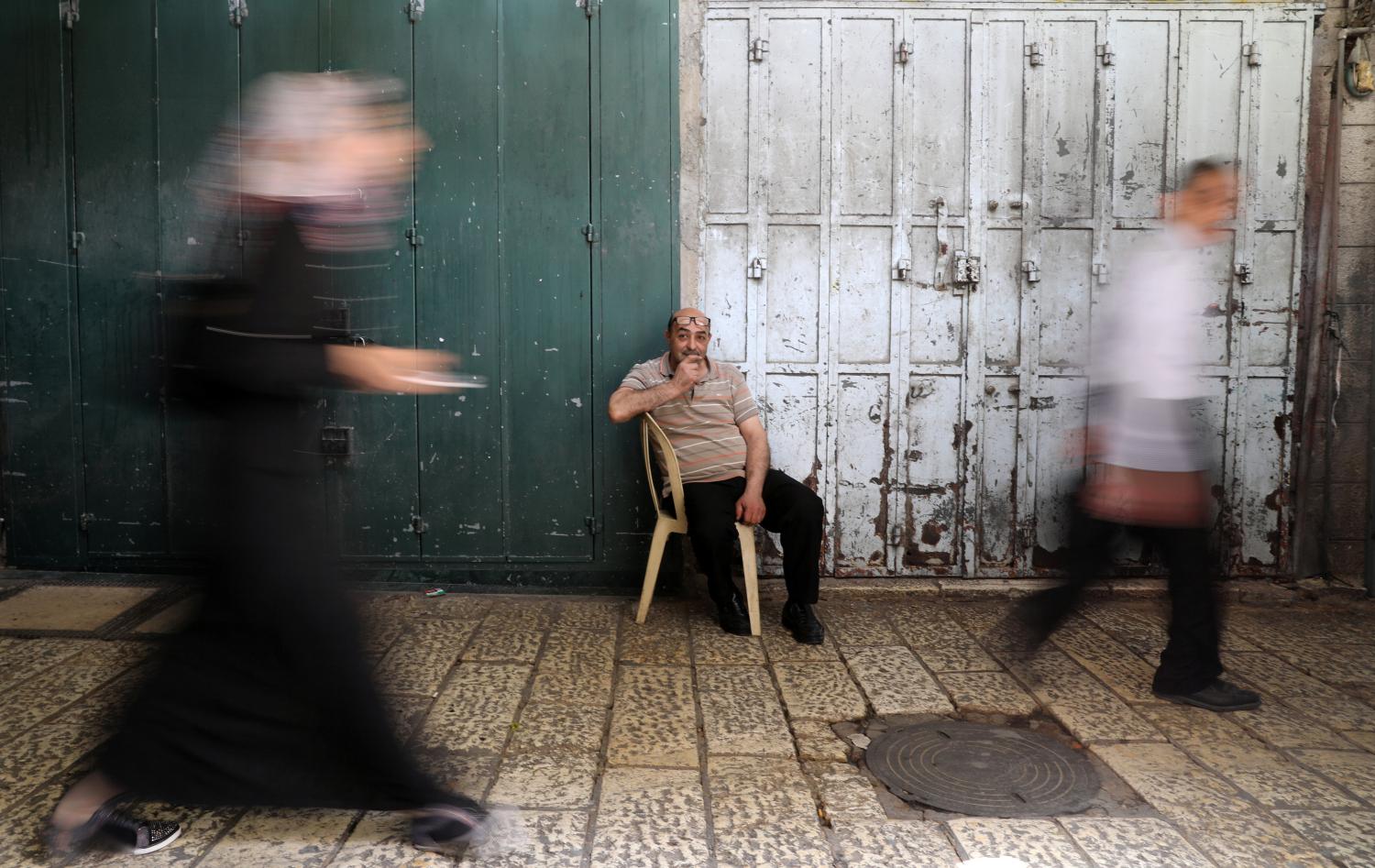 A man sits as people walk past closed shops during a general strike in solidarity with Palestinian prisoners on hunger strike in Israeli jails, in Jerusalem's Old City, April 27, 2017. REUTERS/Ammar Awad - RTS145IT