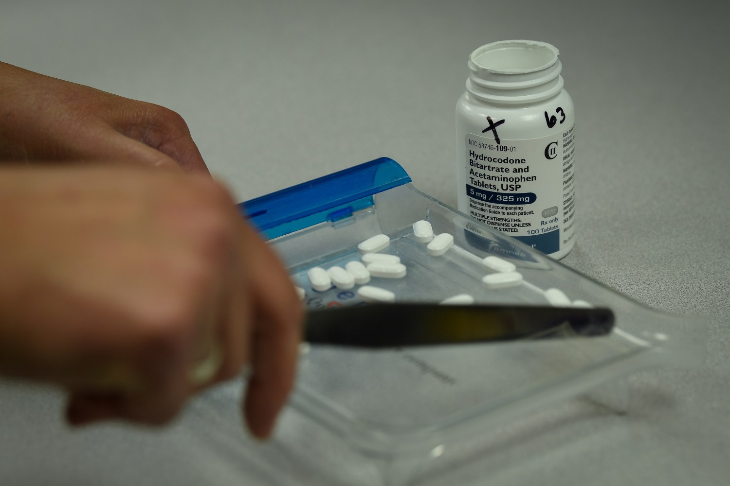 A pharmacist counts tablets of Hydrocodone at a pharmacy.