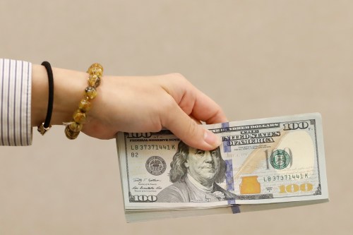 A teller holds U.S. $100 dollar at a bank.