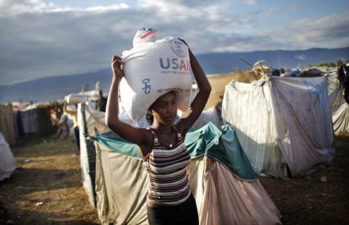 A woman carries a bag of rice from USAID as part of food distributed by various relief agencies in Cite Soleil, Port-au-Prince February 18, 2010. France will provide 270 million euros (US$366.8 million) over two years to Haiti to help the Caribbean nation's economy recover from a devastating January 12 earthquake, France's President Nicolas Sarkozy said on Wednesday. REUTERS/Carlos Barria (HAITI - Tags: DISASTER ENVIRONMENT FOOD SOCIETY POLITICS) - RTR2AI1Z