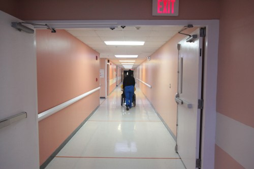 A nurse pushes a patient in a wheelchair through a hall.