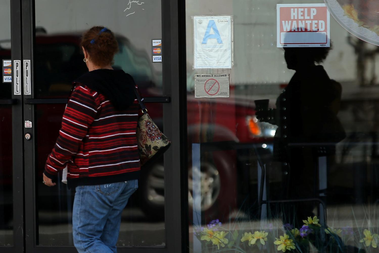 A woman walks past a "help wanted" sign on a restaurant in Los Angeles, California.
