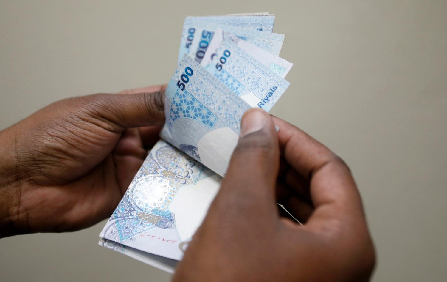 A man counts Qatari riyal notes at a money changer in Doha May 28, 2013. Qatar may change its peg to the U.S. dollar when the economy becomes less dependent on hydrocarbons and local financial markets deepen, although no changes are currently being considered, its central bank chief said. Qatar adopted a currency peg after gaining independence from Britain in 1971. It has kept the riyal pegged at 3.64 riyal to the dollar since 2001. Picture taken May 28, 2013. REUTERS/ Fadi Al-Assaad