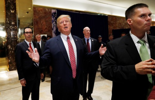 U.S. President Donald Trump stops to respond to more questions about his responses to the violence, injuries and deaths at the "Unite the Right" rally in Charlottesville as he walks away flanked by Treasury Secretary Steven Mnuchin (L) and U.S. Secret Service agents (R) after speaking to the media in the lobby of Trump Tower in Manhattan, New York, U.S., August 15, 2017. REUTERS/Kevin Lamarque - RTS1BXP3