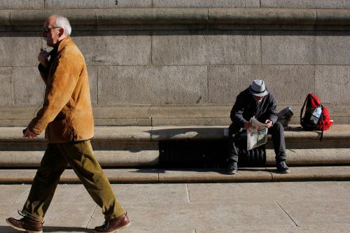 A man sits in the sun reading a newspaper.