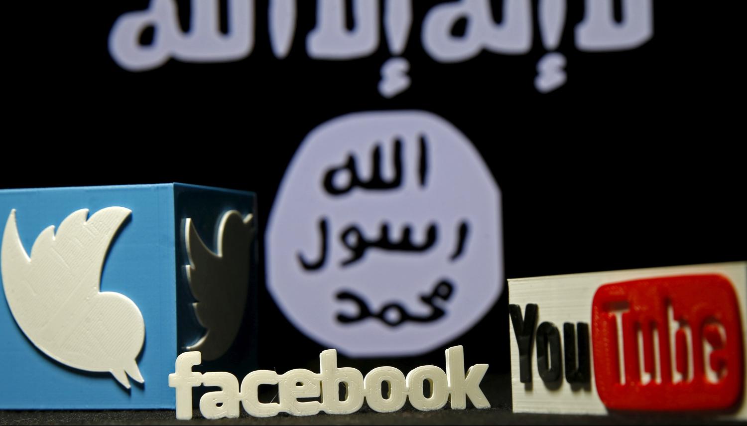 3D plastic representations of the Twitter, Facebook and Youtube logos are seen in front of a displayed ISIS flag in this photo illustration shot February 3, 2016. REUTERS/Dado Ruvic/File Photo - D1BETXLAOLAA