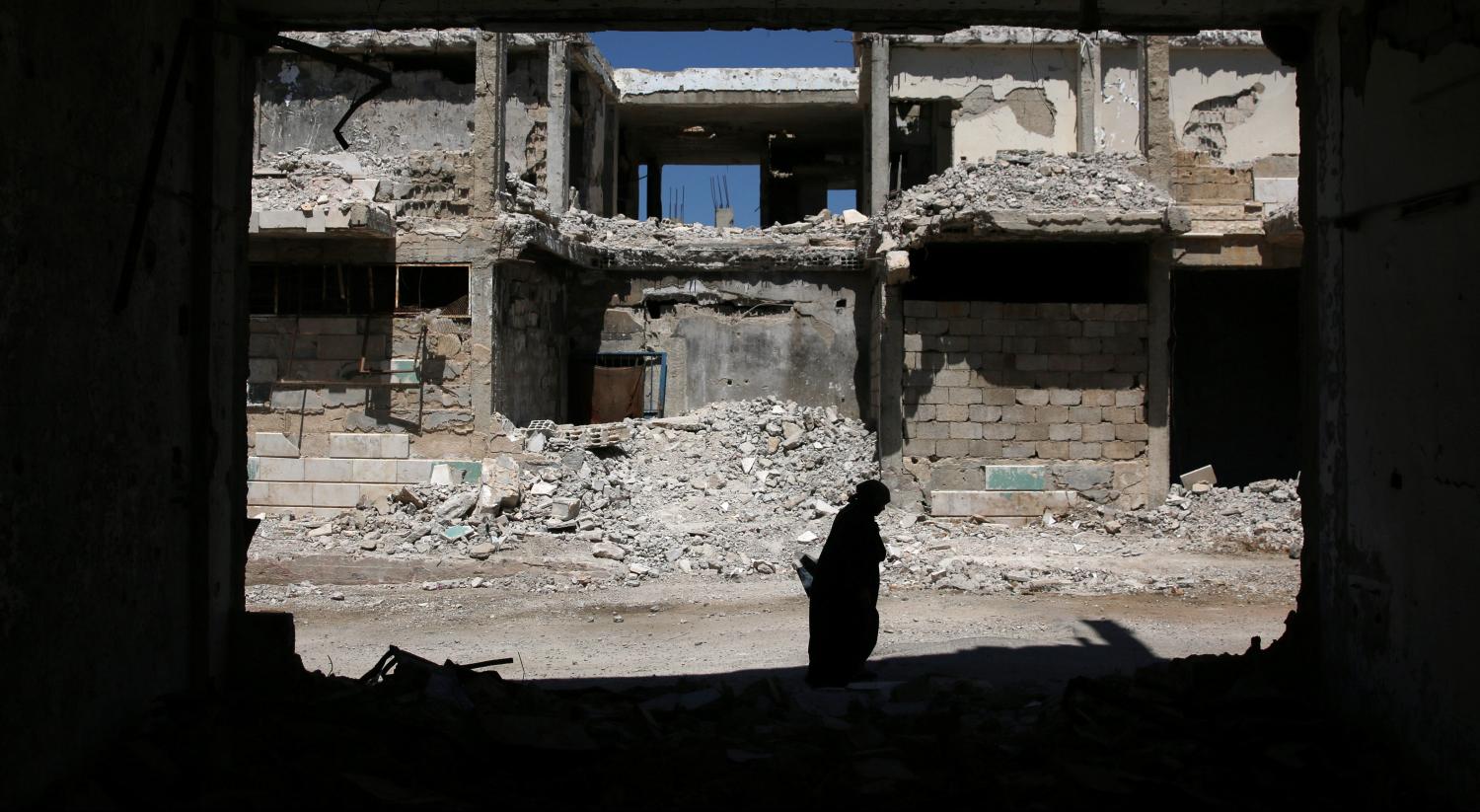 A woman walks past damaged buildings in the rebel-held city of Inkhil, west of Deraa, Syria, September 7, 2017. REUTERS/Alaa Al-Faqir - RC13F5560C30