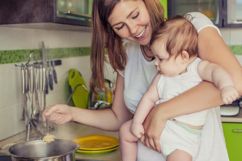 The mother of a woman with a baby cooks the food in a pot on the stove.