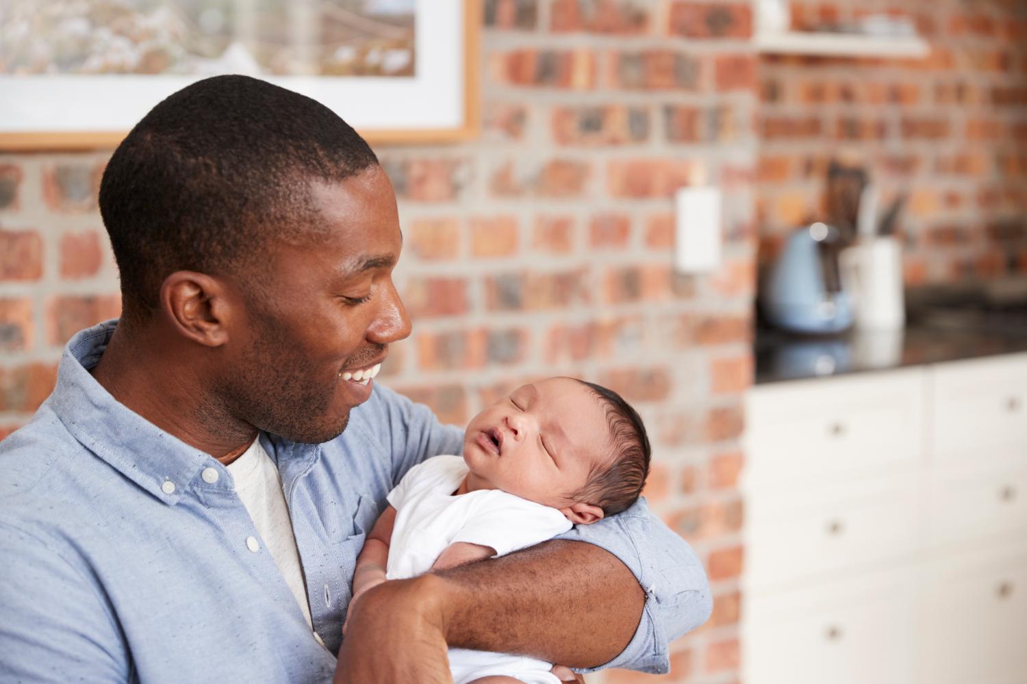 Father At Home Sitting And Holding Newborn Baby Son.