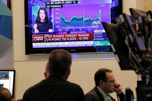 Traders work on the floor of the New York Stock Exchange (NYSE) as a television screen shows news of the announcement that the U.S. Federal Reserve will hike interest rates.