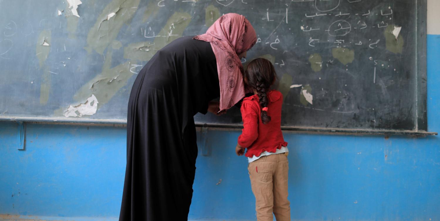 A girl writes on a chalkboard at school.