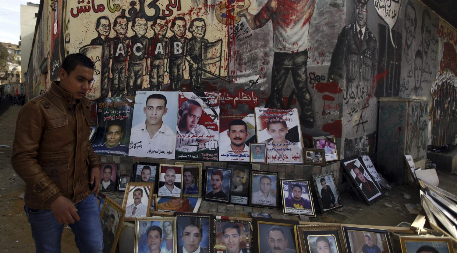 A man walks past photos showing people killed during protests, at Mohamed Mahmoud street in Cairo November 29, 2012. An Islamist-led assembly was expected to finalise a new constitution on Friday aimed at transforming Egypt and paving the way for an end to a crisis which erupted when President Mohamed Mursi gave himself sweeping new powers last week. The street is the location where at least 42 protesters died during clashes in 2011 during Egypt's interim military rule. The graffiti at rear shows an image of ousted president Hosni Mubarak merged with that of Mohamed Hussein Tantawi, the former head of the army council that ruled Egypt, (2nd L), and Muslim Brotherhood leader Mohammed Badie (L). REUTERS/Amr Abdallah Dalsh (EGYPT - Tags: POLITICS) - GM1E8BU0QVE01