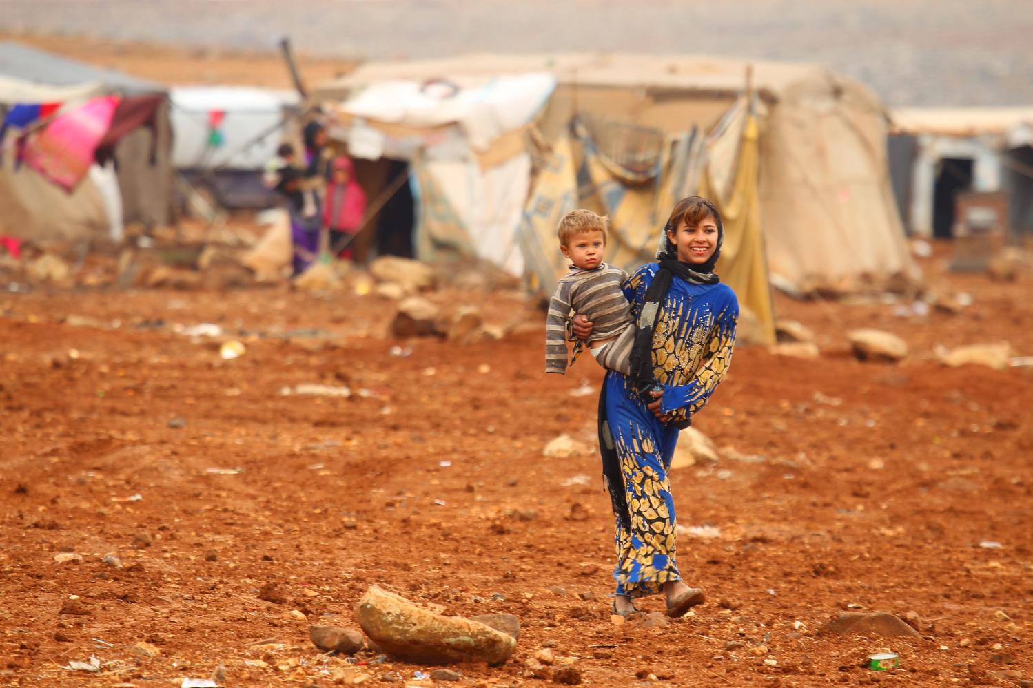 An Internally displaced Syrian youth carries a baby inside a refugee camp in the Hama countryside, Syria January 1, 2016. REUTERS/Ammar Abdullah