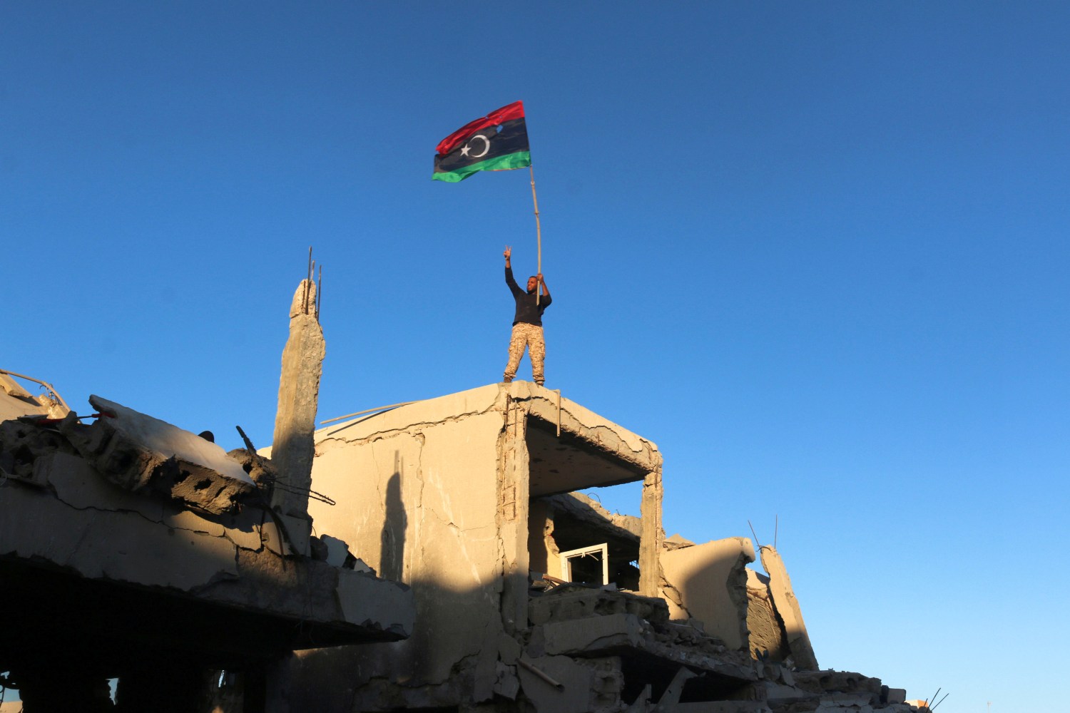 A fighter of Libyan forces allied with the U.N.-backed government waving a Libyan flag flashes victory sign as he stands atop the ruins of a house after forces finished clearing Ghiza Bahriya, the final district of the former Islamic State stronghold of Sirte, Libya December 6, 2016. REUTERS/Hani Amara TPX IMAGES OF THE DAY - RC1FA78AC920