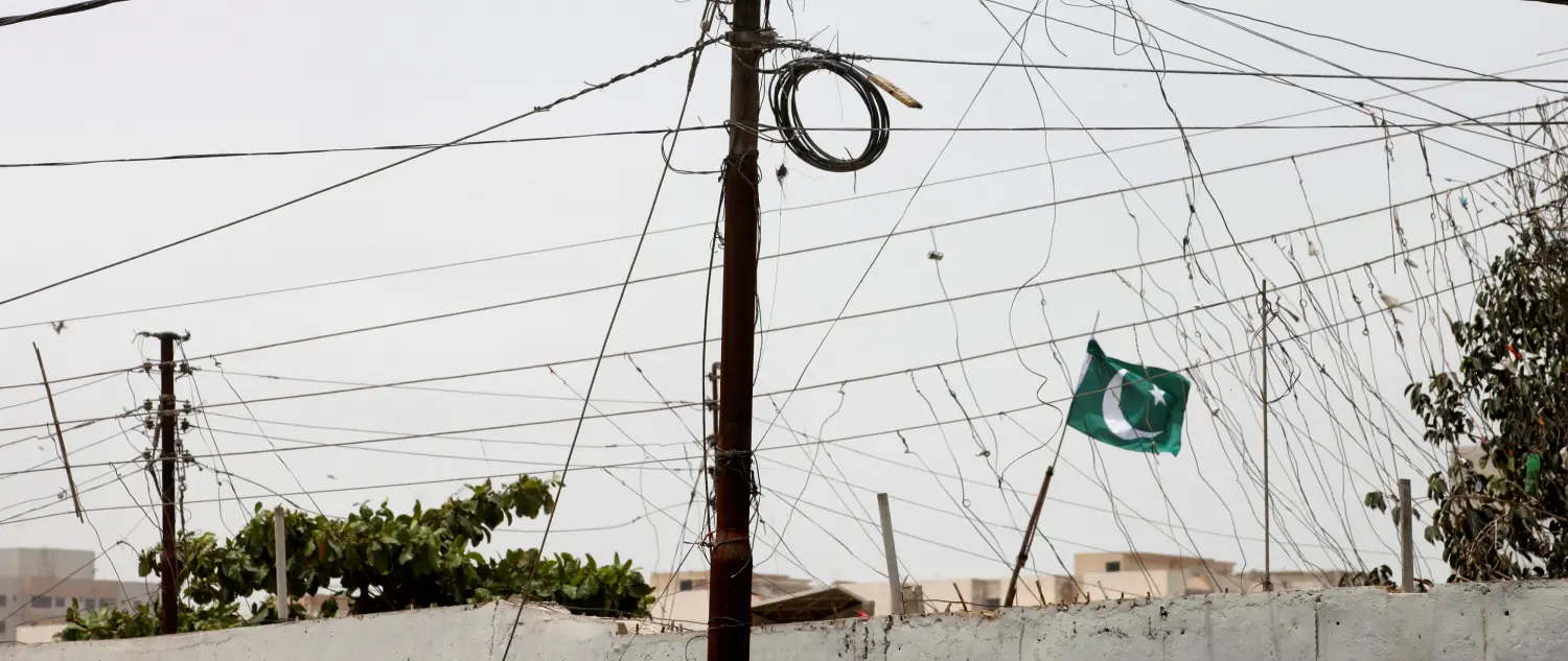 A flag flutters amid cables of illegal electricity connections at a low-income neighborhood in Karachi, Pakistan August 12, 2017. REUTERS/Akhtar Soomro - RC132EB1C580