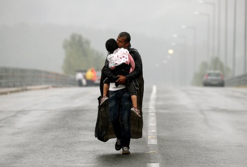 A Syrian refugee carries his daughter through a rainstorm towards the Greek-Macedonian border