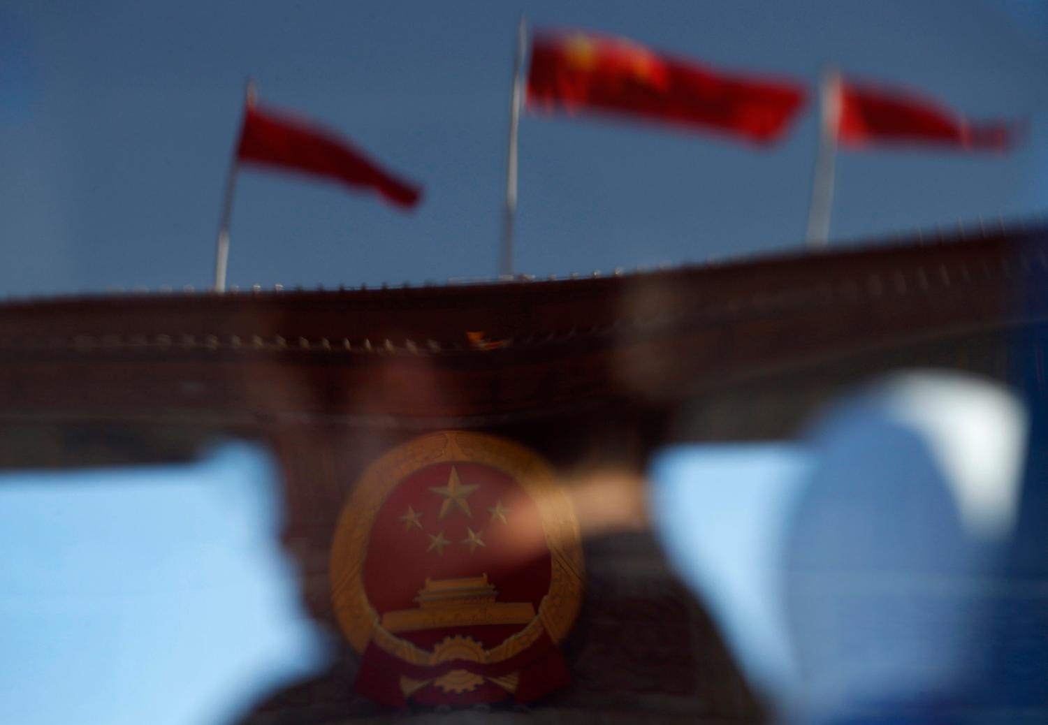 A delegate and the Great Hall of the People, the venue of the 18th National Congress of the Communist Party of China, are reflected in a window of a bus, on Tiananmen Square in Beijing, November 14, 2012.