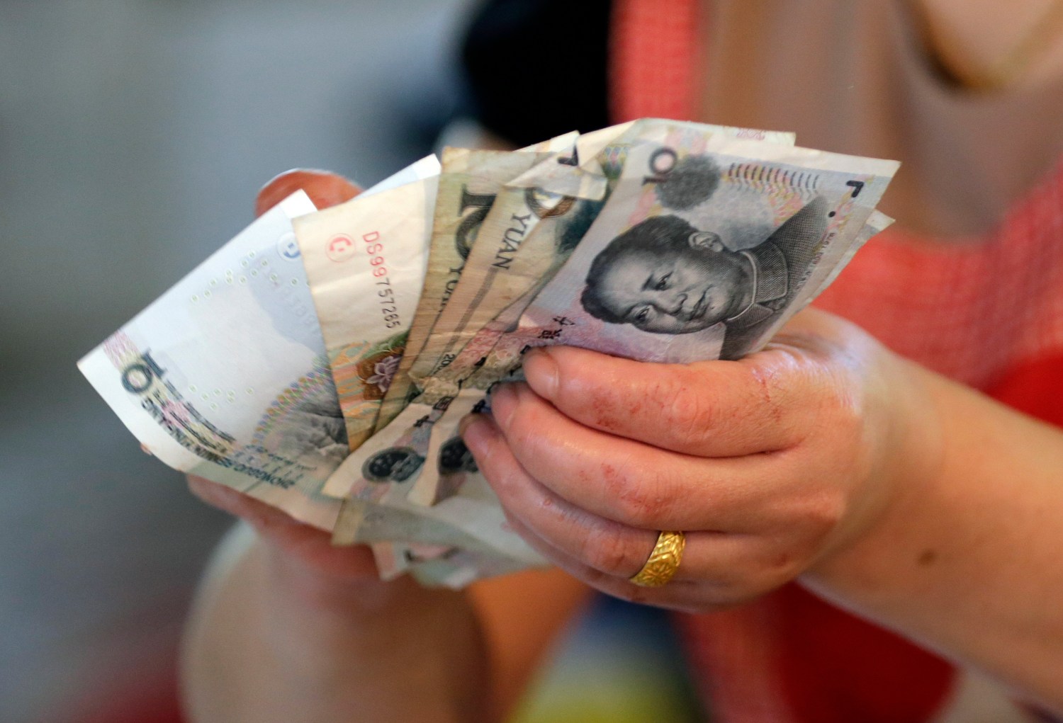 A vendor holds Chinese Yuan notes at a market in Beijing, August 12, 2015. China shocked global markets on Tuesday by devaluing its currency after a run of poor economic data, a move it billed as a free-market reform but which some experts suspect could be the beginning of a longer-term slide in the exchange rate. REUTERS/Jason Lee - SR1EB8C09B142