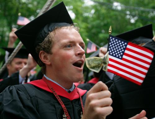 Regan Grabner waves a U.S. flag with a dollar bill tied to it as he graduates from Harvard's Business School during the 357th Commencement Exercises at Harvard University in Cambridge