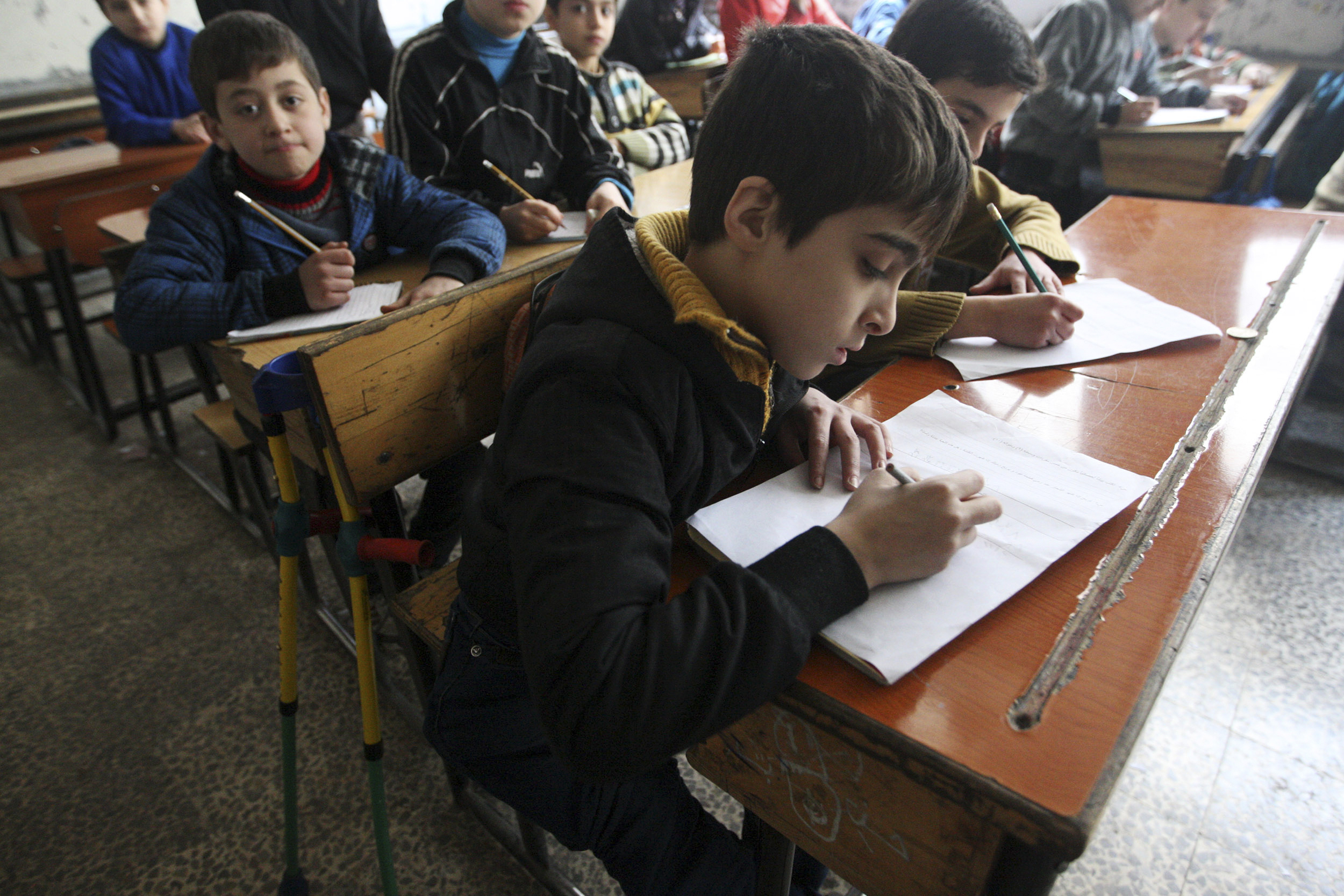 Disabled 11-year-old boy Abdel Jaleel al-Homsy attends a class in Aleppo's Bustan al-Qasr March 12, 2014. Homsy, who was wounded and disabled in 2012 by shelling from forces loyal to Syria's President Bashar al-Assad, has decided to go back to school despite his injuries - helped by Qanawati who accompanies him everywhere. REUTERS/Aref Alkrez    (SYRIA - Tags: POLITICS CIVIL UNREST CONFLICT) - GM1EA3D025Z01