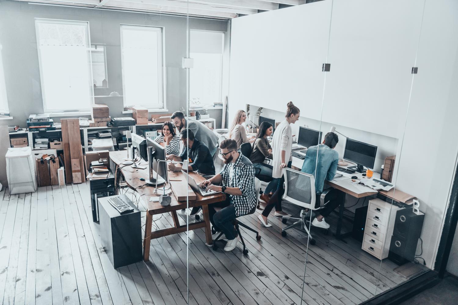 Top view of young modern people in casual wear concentrating at their projects while working together behind the glass wall in the creative office