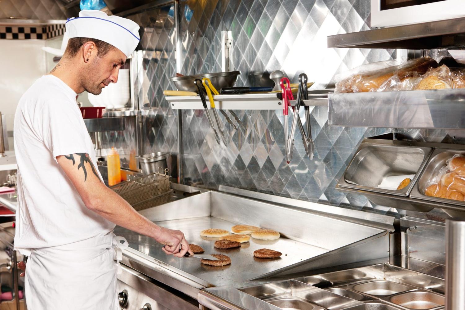 Fry cook cooking burgers in a commercial fast food restaurant kitchen