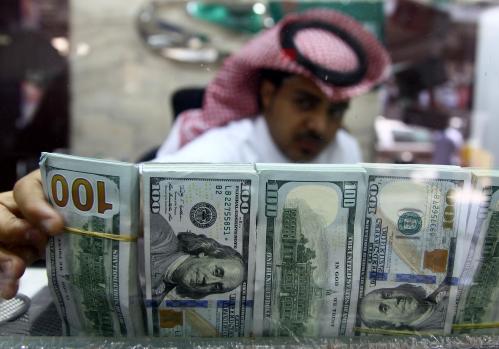 A Saudi money changer, pictured through a glass, arranges U.S banknotes at a currency exchange shop in Riyadh, Saudi Arabia September 29, 2016. REUTERS/Faisal Al Nasser