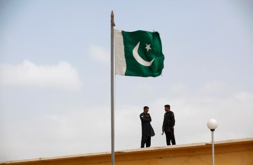 A Pakistani flag flies on a mast in front of paramilitary Frontier Corps soldiers.