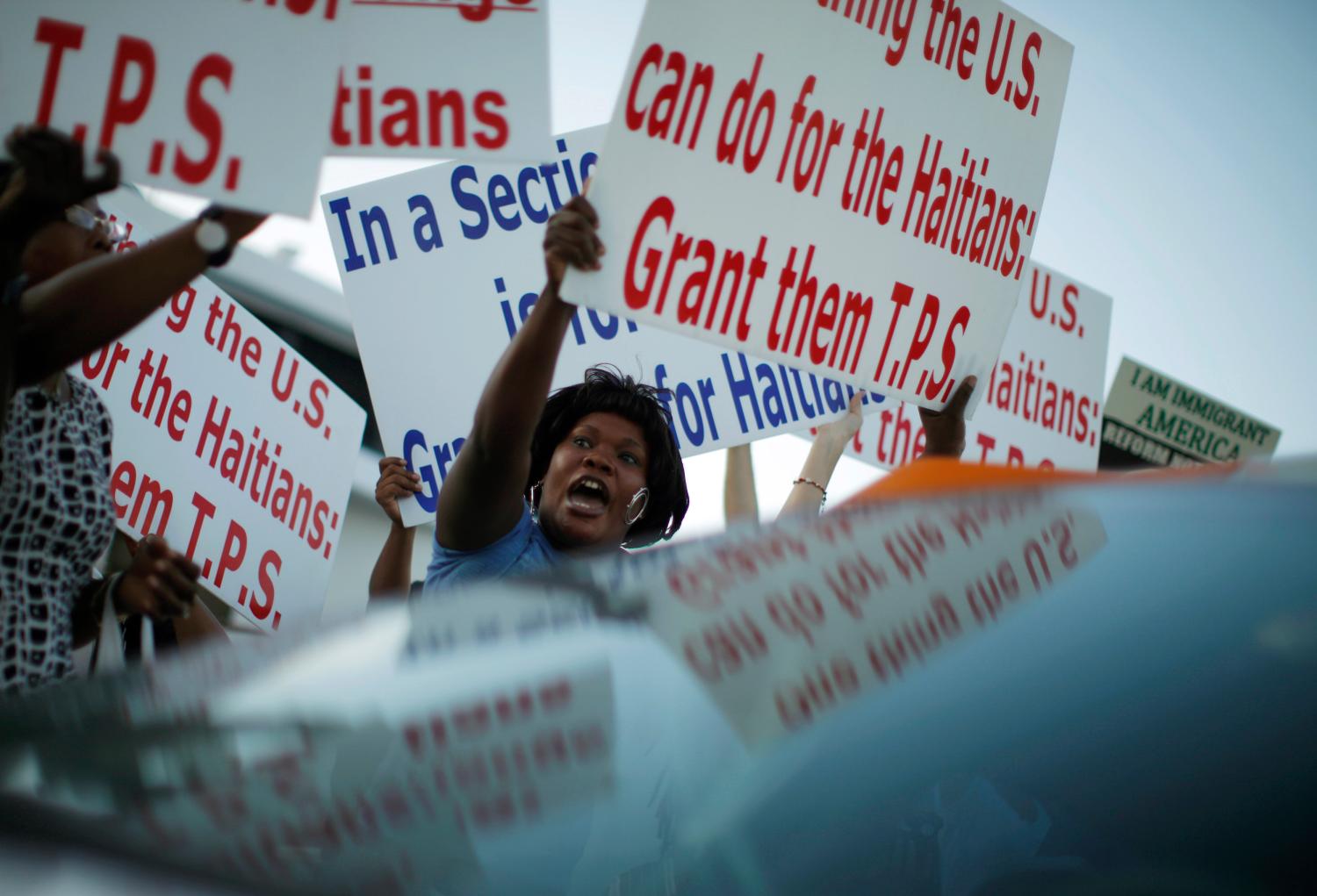Protesters hold up signs in favor of granting Haitian refugees TPS.