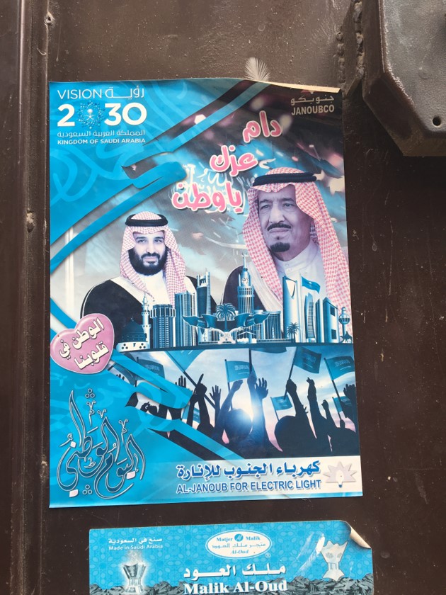 A poster, printed by a local utility company to acclaim the king’s national reform plan, called Vision 2030. Ads for Vision 2030 are omnipresent in Riyadh. We often think of the Kingdom of Saudi Arabia as a religious state, ruled by the Custodian of the Two Holy Mosques, and whose constitution is the shariah. Analysts often describe the state as a grand alliance between the ruling family and the clerical establishment, in which religious legitimacy is central. But one of the interesting features of today’s Saudi Arabia is the way Saudi national identity is being pushed forward as a source of unity and legitimacy. This poster is a good example. The slogan next to King Salman says “May your greatness be infinite, oh nation,” and the heart next to the crown prince says “The nation is in our hearts.”