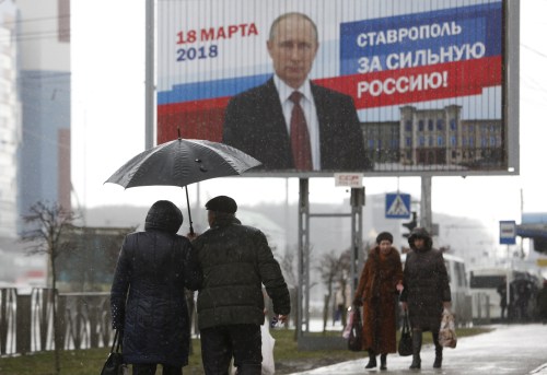People walk next to the election campaign poster of Russian President Vladimir Putin