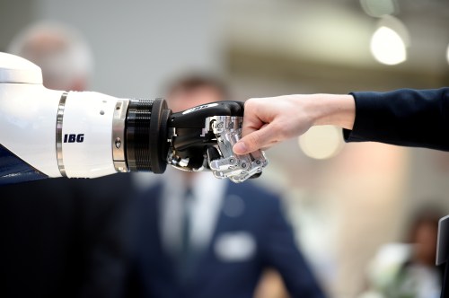 A visitor fist bumps a humanoid robot at the booth of IBG at Hannover Messe, the trade fair in Hanover