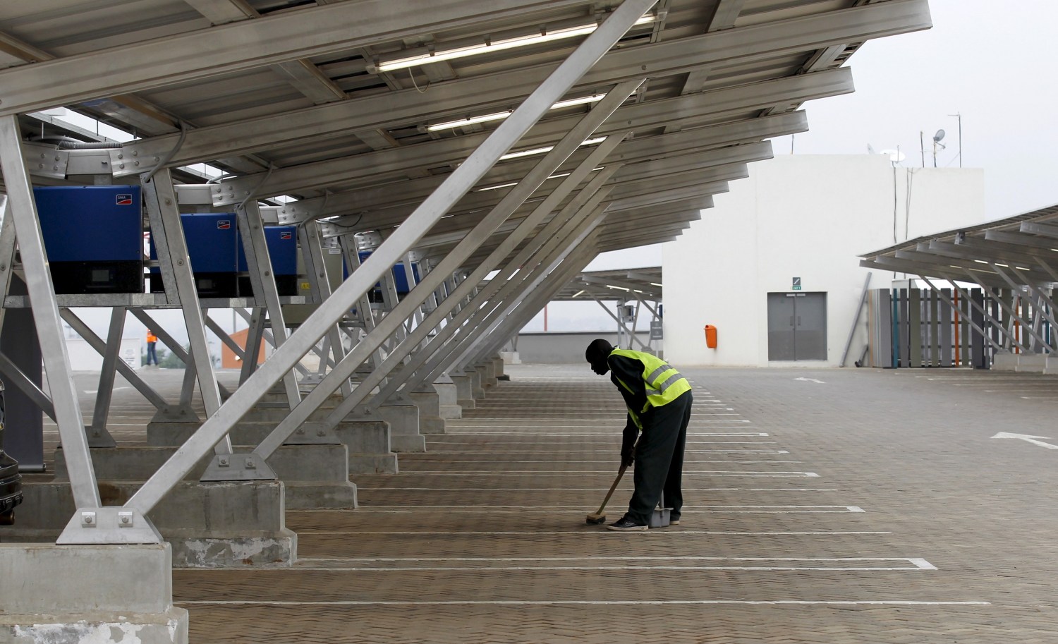 A worker sweeps the floor under solar panels which provide shade for vehicles at a solar carport at the Garden City shopping mall in Kenya's capital Nairobi, September 15, 2015. The Africa's largest solar carport with 3,300 solar panels will generate 1256 MWh annually and cut carbon emission by around 745 tonnes per year, according to Solarcentury and Solar Africa.  REUTERS/Thomas Mukoya - GF10000206552