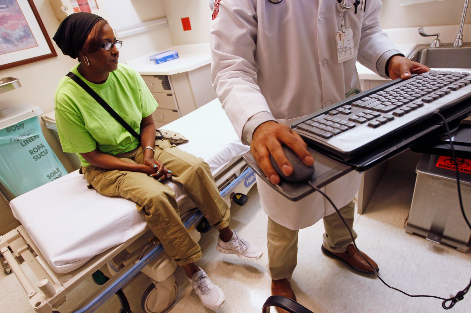 Patient Sharon Dawson Coates (L) waits as Dr. Nikhil Narang enters data into her chart after examining her knee